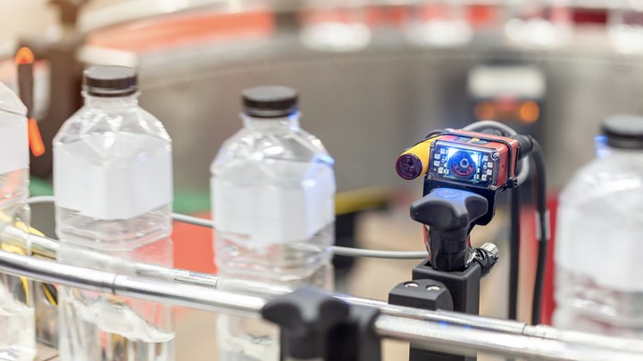 A sensor with a digital screen checks bottles on a conveyor belt.