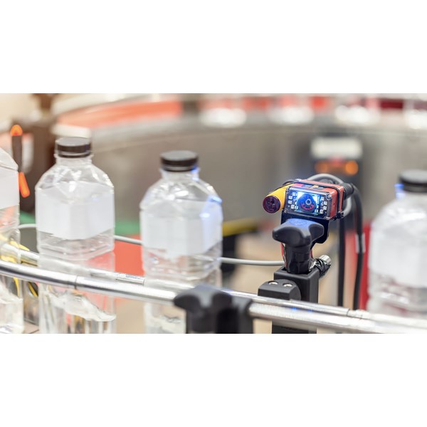 A sensor with a digital screen checks bottles on a conveyor belt.