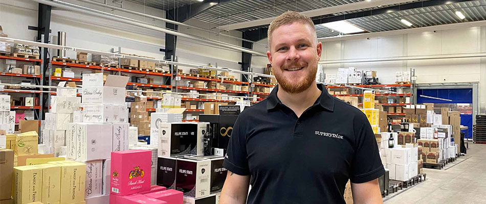 The logistics manager at Supervin poses in front of a wide range of different wines. 